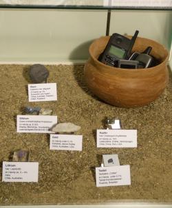 A tárolóban egy régi mobiltelefonokkal teli cseréptálat és telefonalkatrészeket helyeztek el. Vitrine_Recycling